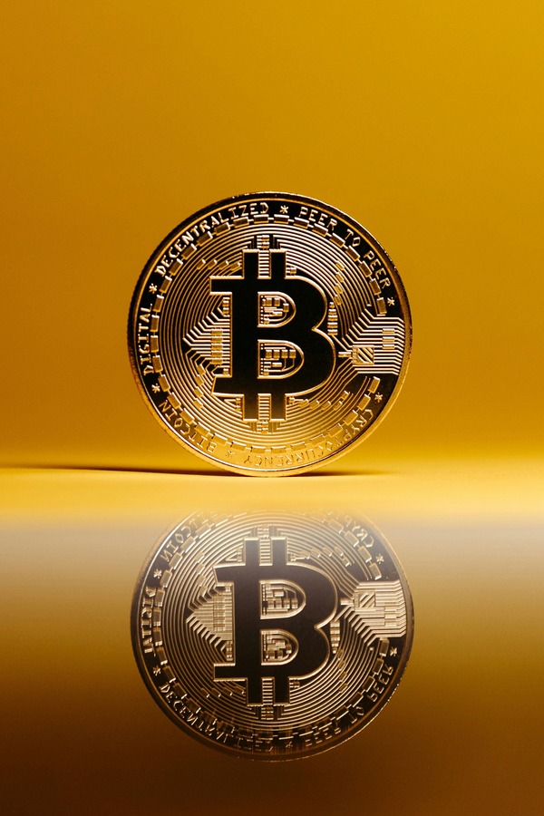 Gold Bitcoin coin standing with a reflection on a glossy surface