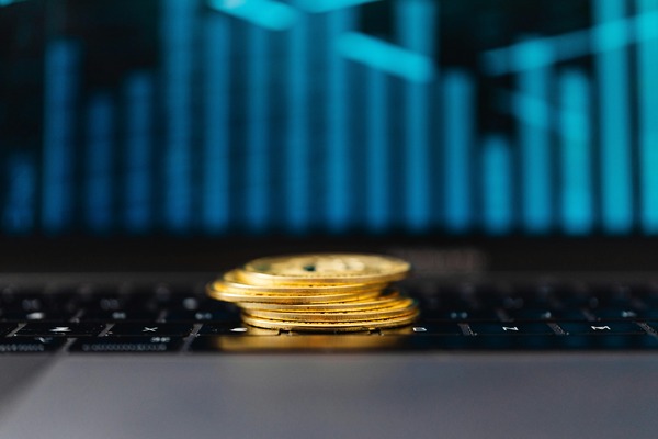 Stack of gold coins on a laptop keyboard with a blue trading chart in the background