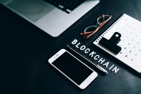 Laptop, phone, and calendar on a desk next to a sign reading blockchain