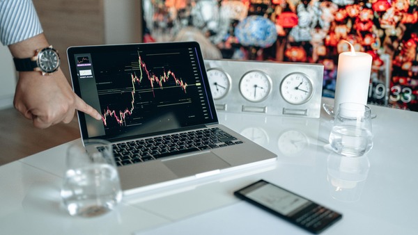 Trader pointing at a candlestick price chart on a laptop next to world clocks